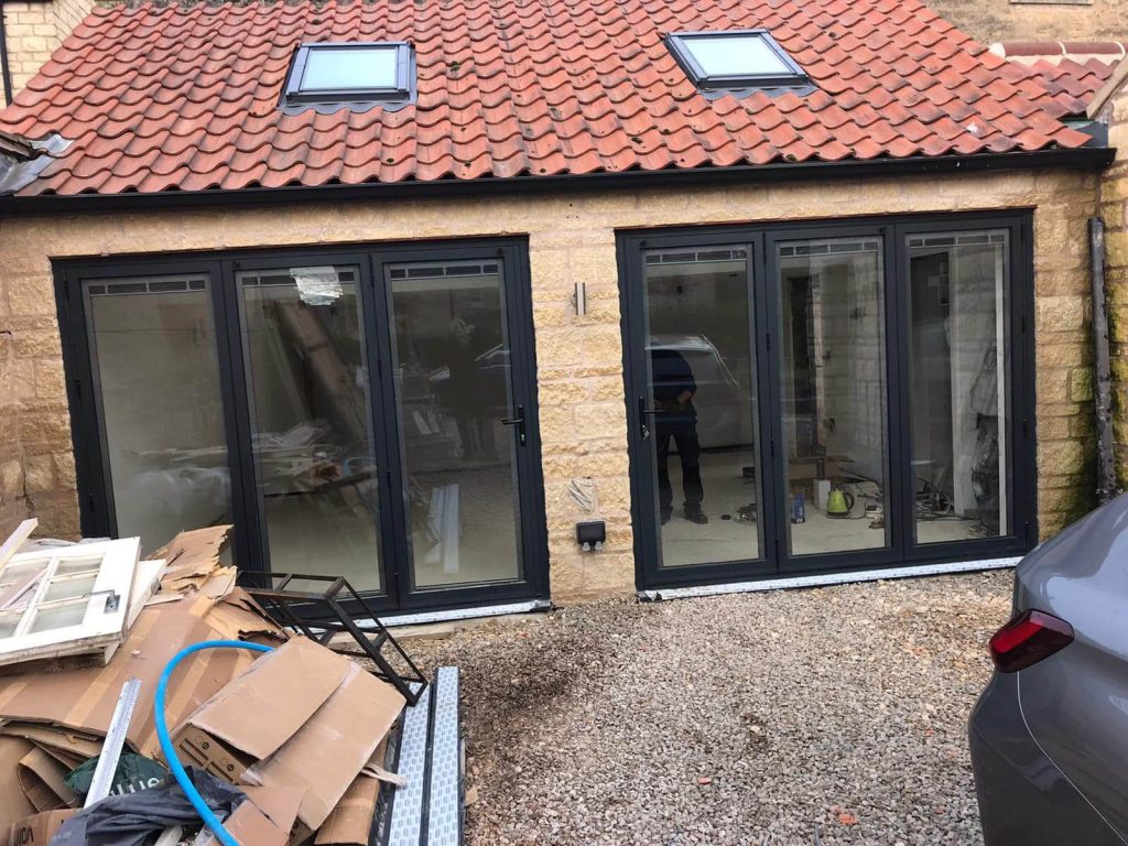 House under construction with the installation of black bifold doors