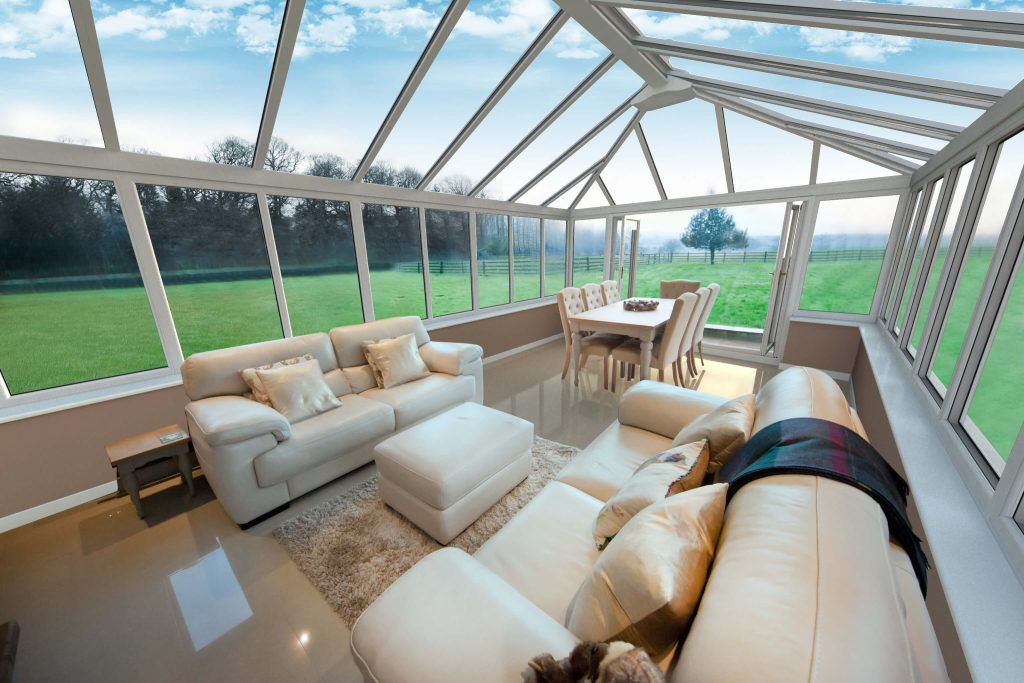 Conservatory with sofas and dining room table, looking open to a large field